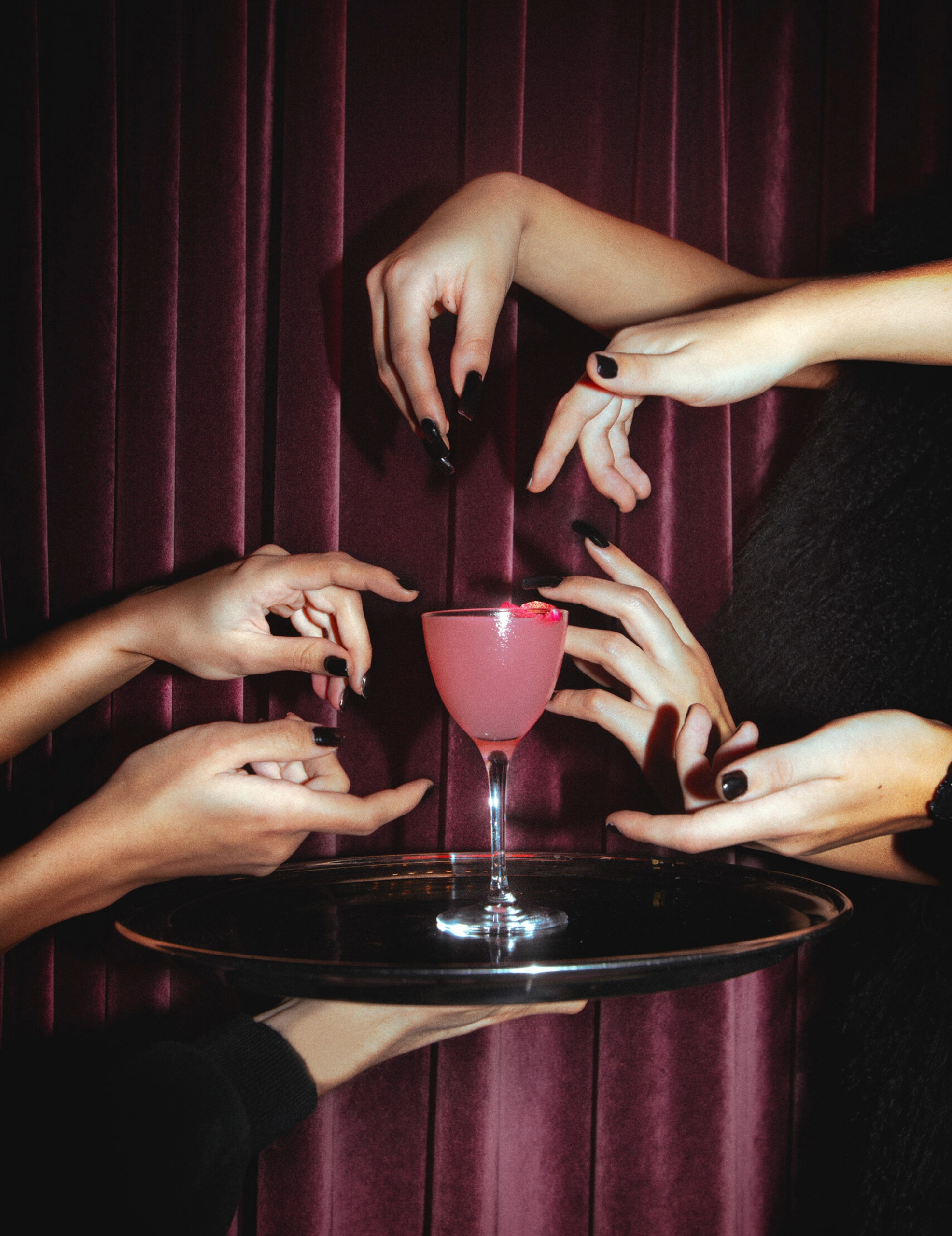 many hands reaching towards a pink drink