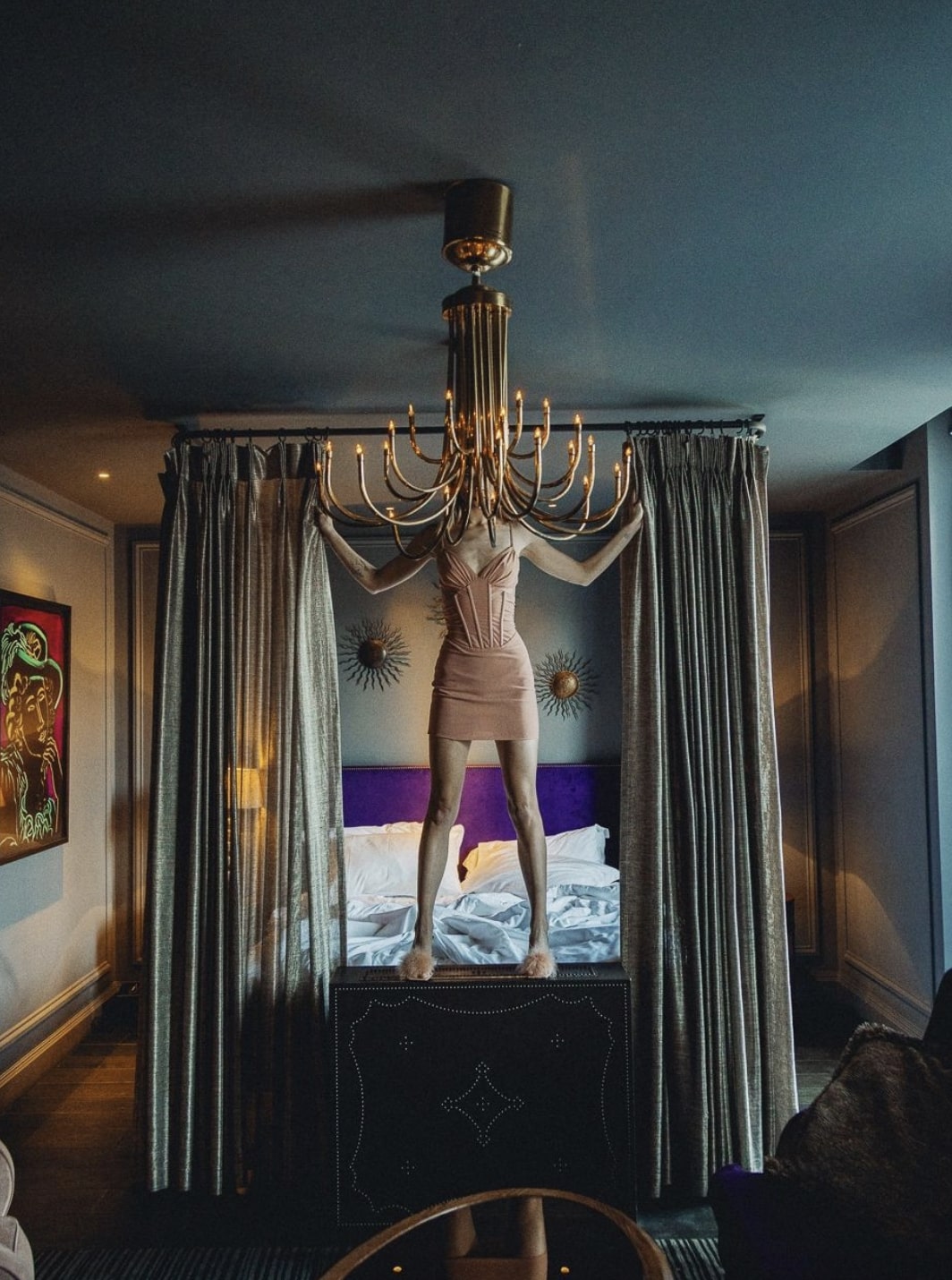 Person standing on bed with face covered by chandelier